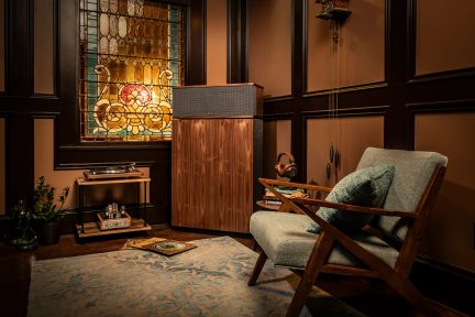 Klipsch hi-fi speaker with black grille and brown wood finish, in a vintage listening room with turntable