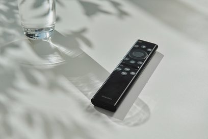 Czarny pilot Samsung leżący na błyszczącej powierzchni obok przezroczystej szklanki wody, widok z góry
