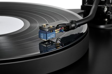 Primo piano di un giradischi nero, braccio metallico con testina blu e fili multicolori su un disco in vinile nero