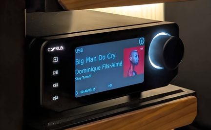 Leitor de áudio hi-fi preto, frontal em vidro, ecrã a cores, botões à esquerda, roda retroiluminada à direita, vista de viés
