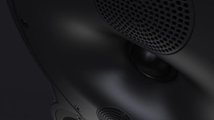 Superficie negra mate con rejillas perforadas circulares, altavoz visible, curvas suaves, tornillo visible, ángulo cercano