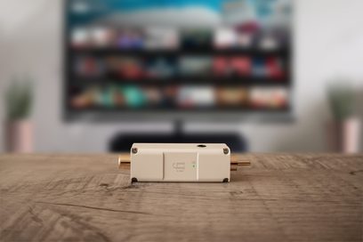 iFi Audio SPDIF iPurifier2 hvidt lydtilbehør, set forfra, placeret på en træoverflade foran en tændt tv-skærm