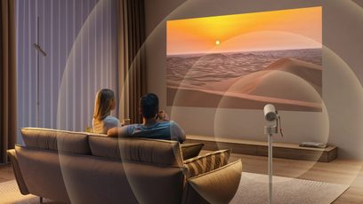 Videoproiettore XGIMI MoGo 3 Pro su supporto, salotto con divano, 2 persone di spalle, proiezione paesaggio deserto, tende, lampada