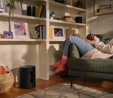Nappali, matt fekete hengeres mélyláda oldalsó nyílásokkal, fapadló, zöld szövet kanapé