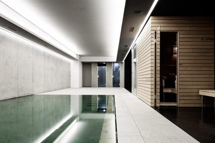 Indendørs designerpool med vægge i rå beton, lyst flisebelagt gangareal og sauna i lyst træ med indirekte LED-belysning