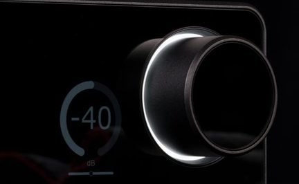 Stor svart metallvolumknapp med hvit lysring, på blank svart front, -40 dB visning, nærbilde