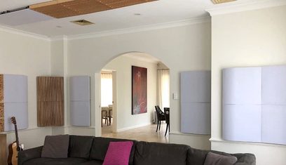 Modernt inre med grå soffa, vita väggar, parkettgolv, stora fönster, abstrakt röd tavla och beige akustikpaneler i hörnen