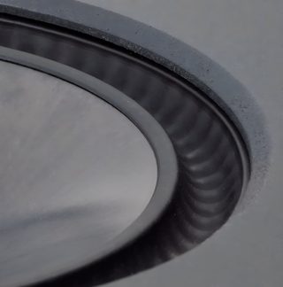 Black textured circular surface with a wavy annular edge, close-up view at an inclined angle, visible details of the relief