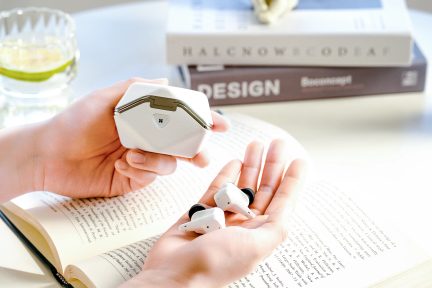 Чоловік тримає білий чохол і білі навушники на відкритій книзі, склянку з жовтою рідиною та книги на задньому плані