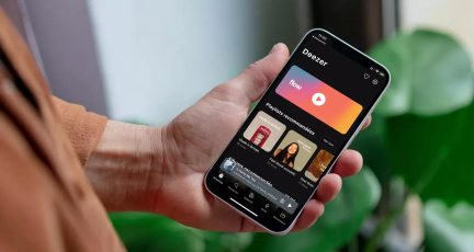 Venstre hånd holder smartphone, der viser musikapplikation, skærm tændt, sløret baggrund med grøn plante