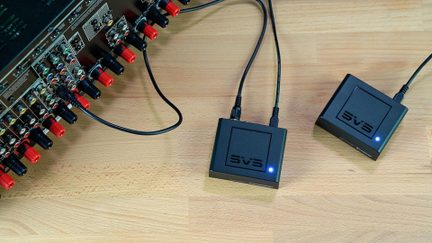 Bezdrátová audio sada vysílač/přijímač SVS připojená k domácímu kinu zesilovači na světlém dřevěném stole