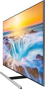 Samsung QE55Q85R-tv, der viser et vandfald omgivet af klipper, med en orange solnedgang i baggrunden