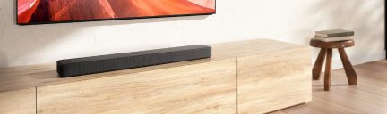 Mueble de madera clara con barra de sonido negra, televisor de pared, taburete de madera, libros apilados, suelo de madera