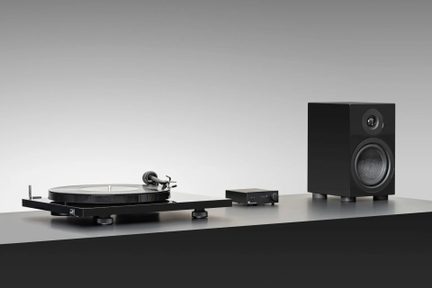 Tocadiscos de vinilo negro con preamplificador compacto y altavoz de estantería negro sobre fondo gris