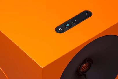 Leuchtend orangefarbener Cambridge Audio L/R Smart-Lautsprecher, Draufsicht, schwarze Touch-Bedienelemente und seitlicher schwarzer Lautsprecher