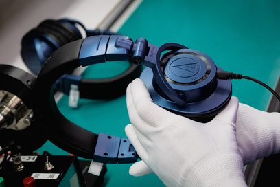 Sluchátka Audio Technica ATH-M50xBT2DS v černé a modré barvě, detailní pohled z levého profilu, položená na bílé rukavici