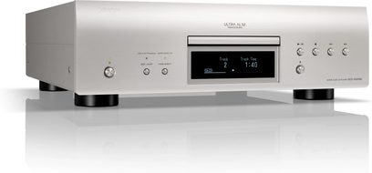 Lettore CD hi-fi DCD-3000NE argento, vista frontale con angolazione leggera, chassis rettangolare, piedini cilindrici neri, display digitale centrale che mostra le informazioni di riproduzione, cassetto del disco sopra il display, pulsanti circolari e indicatori luminosi a sinistra, comandi di riproduzione a destra.
