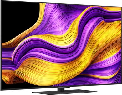 LG OLED65G5 2025 sort tv med ultratynd metalramme og glas-skærm, der viser et abstrakt lilla og gult mønster, monteret på en lav, rektangulær fod, set fra venstre trekvart vinkel