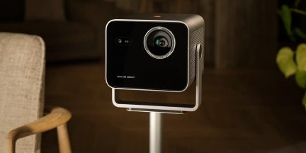 Juodas Leica Cine Compact vaizdo projektorius su blizgiu priekiniu skydeliu ir priekiniu objektyvu ant stovo, trijų ketvirčių vaizdas