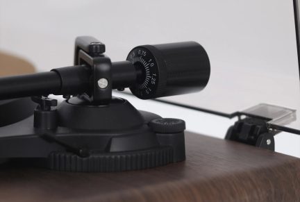 Sort tonearm til pladespiller med gradueret kontravægt, i nærbillede på en brun sokkel