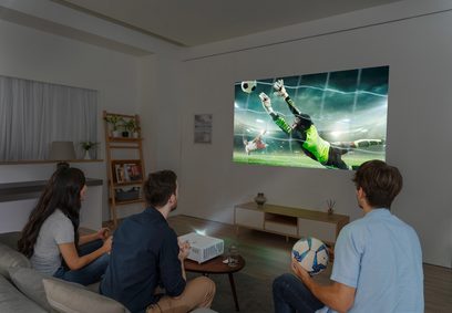 Optoma UHZ50 projektor, der viser en fodboldkamp på et lærred, set af en familie, der sidder i en sofa