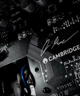 Placă de circuit imprimată neagră cu componente electronice, cu semnătura "R-line" gravată și textul "CAMBRIDGE" alb