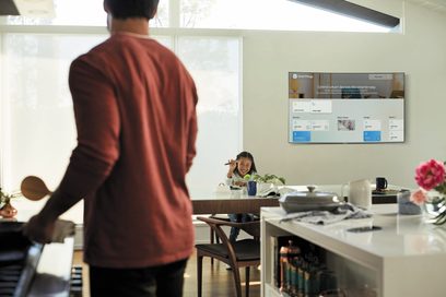 Samsung QE65Q8C 2018-fjernsyn, der viser SmartThings-grænsefladen, en kvinde sidder ved et bord i et køkken