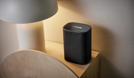 Compacte zwarte draadloze Canton-luidspreker met afgeronde hoeken, op een nachtkastje van licht hout met een witte lamp