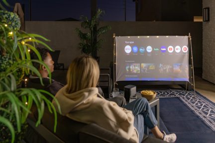 Schermo di proiezione da esterno su supporto con ghirlanda luminosa, installazione cinema in terrazza