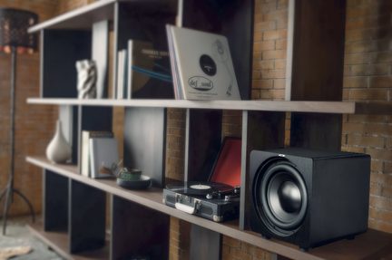 Zwarte subwoofer op een houten plank, naast een platenspeler en platen, loftdecor in baksteen