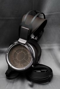 Cuffia hi-fi aperta STAX SR-X9000 nera, vista di tre quarti frontale, appoggiata su cavo arrotolato, trasduttori circolari argentati