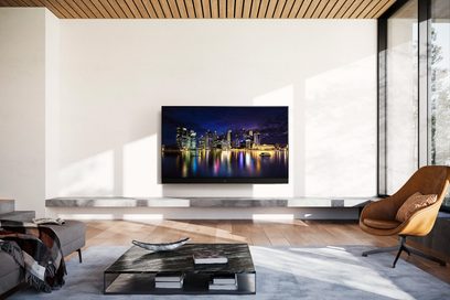 Téléviseur Panasonic TX-65MZ2000E affichant une vue nocturne de gratte-ciels illuminés au bord de l'eau, dans un salon moderne