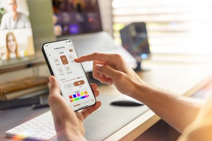 Smartphone, der viser ProMedia Lumina-appen til styring af tilsluttet belysning, i et moderne lyst kontor