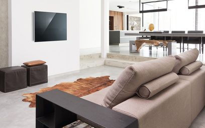 Moderne stue med beige sofa, brune puder, skindstæppe, sort sofabord, vægmonteret tv og stort vinduesparti