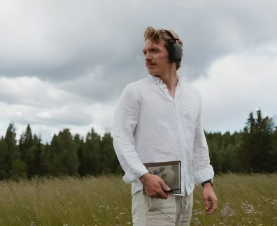 Fones de ouvido sem fio pretos usados por um homem de camisa branca em um campo sob um céu nublado