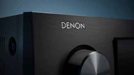 Černý zesilovač Denon v detailním pohledu s kartáčovaným čelním panelem a velkým kruhovým ovladačem hlasitosti
