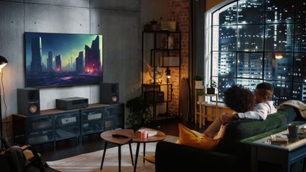 Sala moderna com sofá verde, mesa de centro redonda, televisão de parede, alto-falantes, estante, grande janela, vista noturna urbana