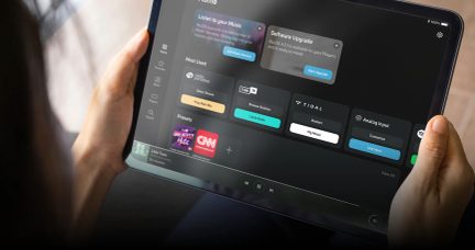Tablični računalnik v rokah s temnim vmesnikom pretakanja glasbe BluOS in storitvami Tidal, TuneIn, Spotify