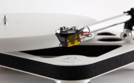 Sølvfarvet tonearm med gennemsigtig gul pickup, farvede kabler, hvid pladetallerken og sort base med synligt logo