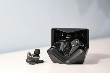 Čierne bezdrôtové slúchadlá do uší s otvoreným nabíjacím puzdrom a jedným slúchadlom položeným vedľa