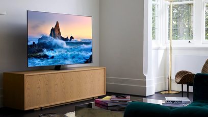 Samsung QE65Q80T 2020 fladskærms-TV, der viser et billede af klipper i et oprørt hav, stående på et lyst trækabinet