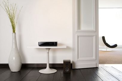 Moderne, minimalistisk indretning med hvid vase, grøn plante, hvidt sofabord, sort Pioneer PDX-Z9 Blu-ray-afspiller, sort lænestol og hvide paneler
