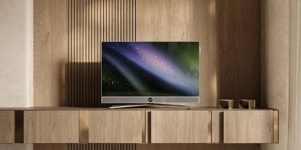 Srebrny telewizor z płaskim ekranem na meblu z jasnego drewna, widok z przodu, z centralną podstawą i zintegrowanym soundbarem