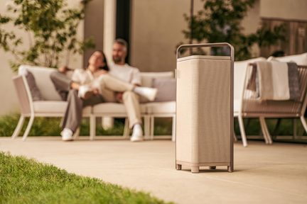 Bärbar utomhus Bluetooth-högtalare i beige tyg på terrass framför avkopplande par i trädgårdssofa