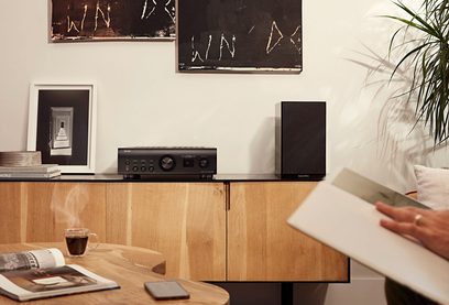 Stereo hi-fi zesilovač Denon PMA-1700NE černý, reproduktory, abstraktní obrazy, rostlina, kniha, mobilní telefon na dřevěném nábytku