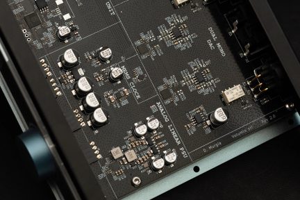 Placă electronică neagră din fibră de sticlă cu condensatori cilindrici argintii, circuite integrate negre și conectori cu pini, vedere oblică de sus