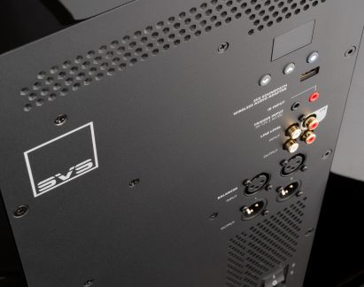 Černý zadní panel s pozlacenými audio konektory RCA, XLR porty, ventilačními mřížkami a bílým logem v levém horním rohu