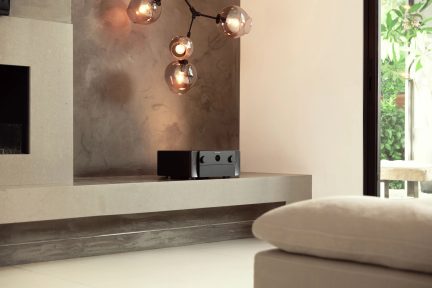Moderne interiør med teksturert vegg, hengende sfærisk lysarmatur, lavt møbel, høyttaler og puter på en sofa