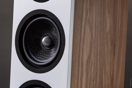 Nærbilde av en høyttaler med hvit front, teksturert svart sirkulær høyttaler og sidepanel i synlig treverk.