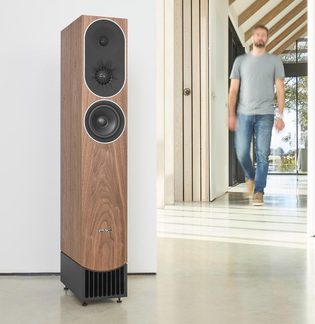 PMC floorstanding speaker with walnut veneer, dual black drivers and a slatted front port in a bright living room